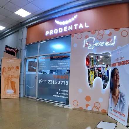 Frente de una sucursal de Prodental dentro de una galería, con el cartel iluminado y la vidriera con la palabra ¡Sonreí!