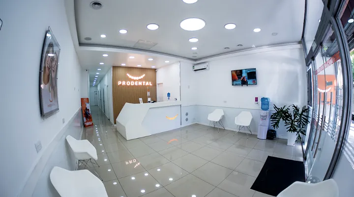 Sala de espera amplia con sillas blancas y la recepción con el cartel PRODENTAL al fondo