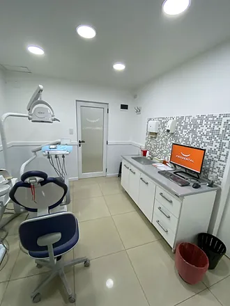 Consultorio con sillón azul, mesada con monitor y pared de venecitas
