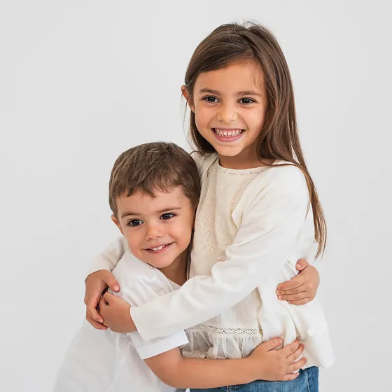 Una nena y un nene abrazados y sonriendo, sobre fondo claro