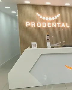 La recepción de una sucursal de Prodental, con el logo iluminado en la pared de madera