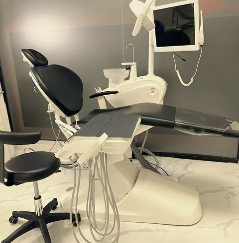 Unidad dental con sillón negro, monitor y taburete sobre piso de mármol, en un consultorio de la clínica