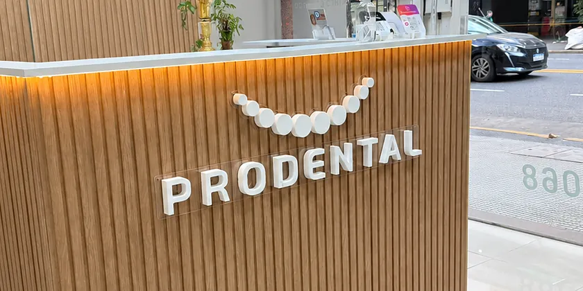 Recepción de Prodental con el mostrador de listones de madera iluminado desde abajo, el logo de la sonrisa y la palabra PRODENTAL