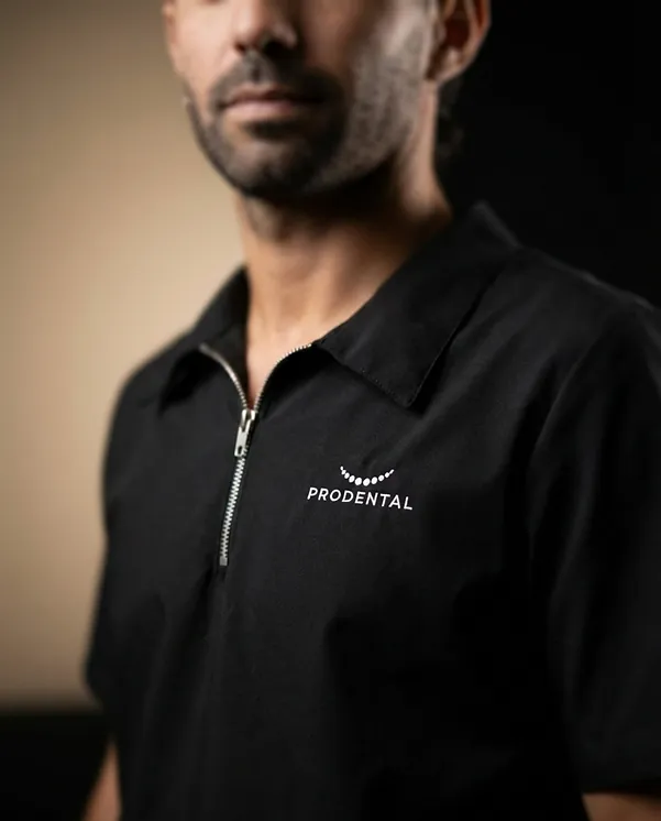 Profesional de Prodental con la chaqueta negra del uniforme, con el cierre al cuello y el logo de la clínica bordado en blanco